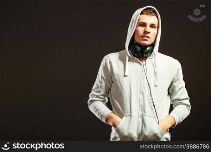 Headshot young handsome hooded man with headphones listening to music black background