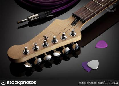 Headstock of electric guitar, jack cable and picks. Close up on the headstock of electric guitar, picks and jack cable next to it, glossy background with reflection