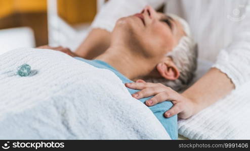 Healing and Balancing Chakras Therapy. Beautiful elderly woman lying on massage table and enjoying chakra healing treatment. Chakra Healing Treatment