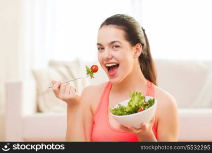 healt, dieting, home and happiness concept - smiling sporty teenage girl with green salad at home