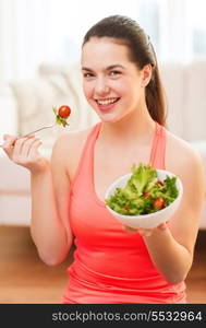 healt, dieting, home and happiness concept - smiling sporty teenage girl with green salad at home