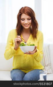 healt, dieting, home and happiness concept - smiling young woman with green salad at home