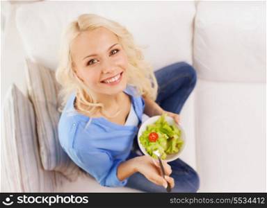 healt, dieting, home and happiness concept - smiling young woman with green salad at home