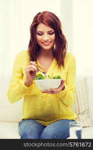 healt, dieting, home and happiness concept - smiling young woman with green salad at home