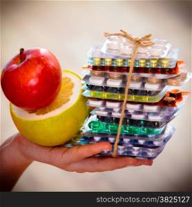 Health and balanced diet concept. Choice between two sources of vitamins - pills or fruits. Closeup female hand holding stack of drugs apple and grapefruit