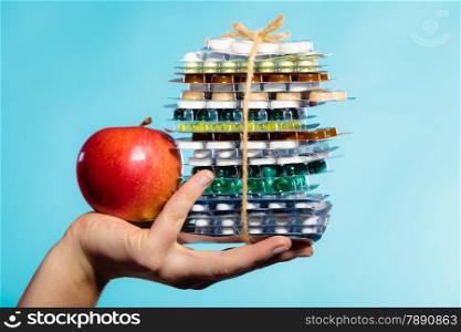 Health and balanced diet concept. Choice between two sources of vitamins - pills or fruits. Closeup female hand holding stack of drugs and apple on blue.