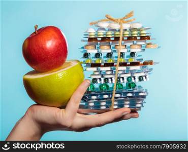 Health and balanced diet concept. Choice between two sources of vitamins - pills or fruits. Closeup female hand holding stack of drugs apple and grapefruit on blue.