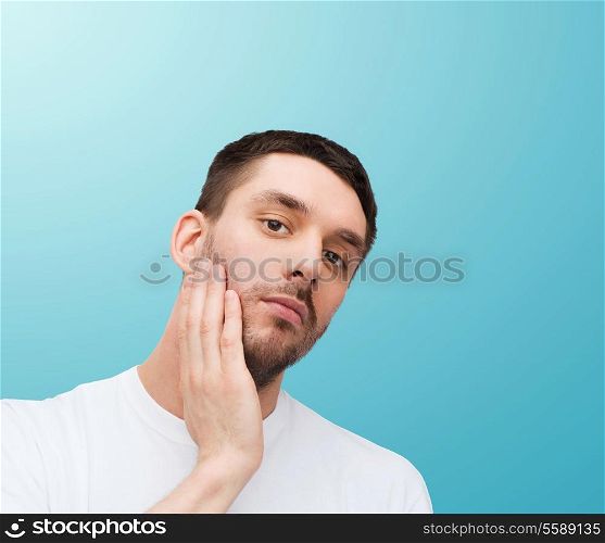 health and beauty concept - beautiful calm man touching his face