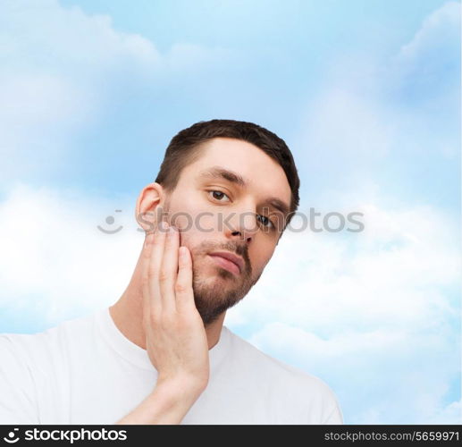 health and beauty concept - beautiful calm man touching his face