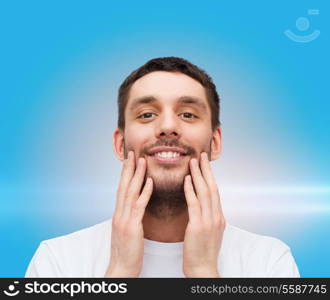 health and beauty concept - beautiful smiling man touching his face