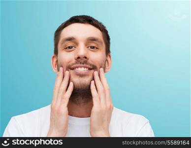 health and beauty concept - beautiful smiling man touching his face