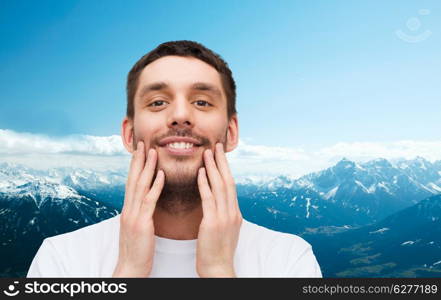 health and beauty concept - beautiful smiling man touching his face