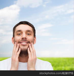 health and beauty concept - beautiful smiling man touching his face