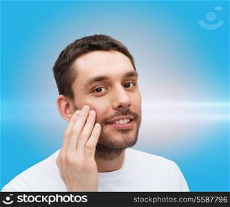 health and beauty concept - beautiful smiling man touching his face or applying cream