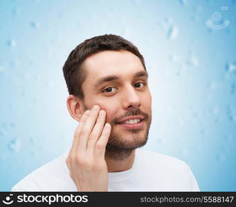 health and beauty concept - beautiful smiling man touching his face or applying cream