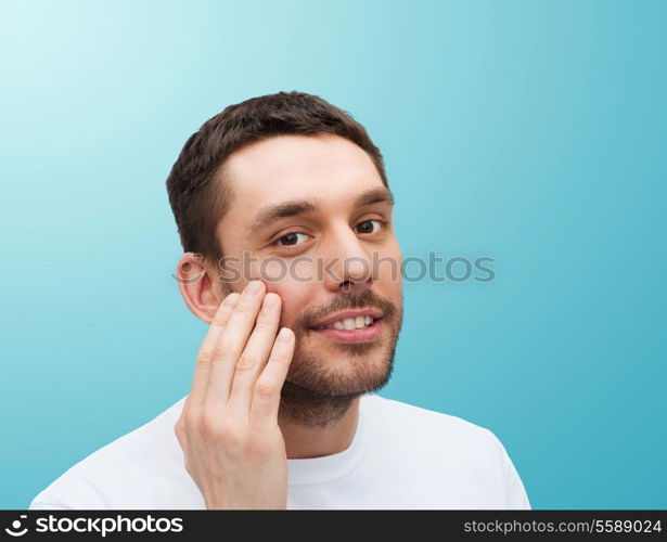 health and beauty concept - beautiful smiling man touching his face or applying cream