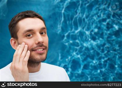 health and beauty concept - beautiful smiling man touching his face or applying cream