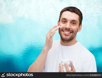 health and beauty concept - beautiful smiling man with jar of cream applying cream