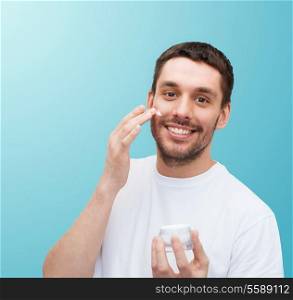 health and beauty concept - beautiful smiling man with jar of cream applying cream