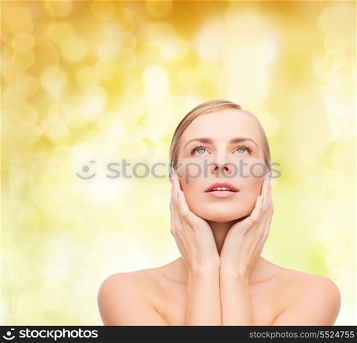 health and beauty concept - beautiful young woman touching her face and looking up