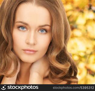 health and beauty concept - face and hands of beautiful woman with long hair over yellow autumn leaves background