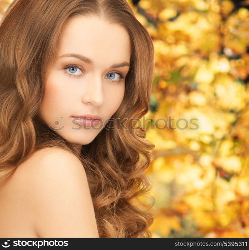 health and beauty concept - face of beautiful woman with long hair over yellow autumn leaves background