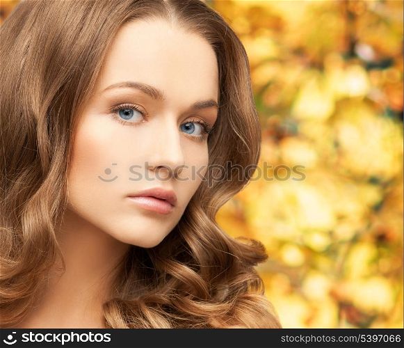 health and beauty concept - face of beautiful woman with long hair over yellow autumn leaves background