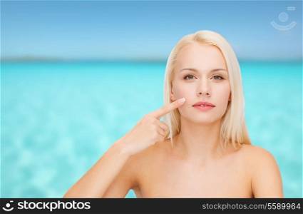 health and beauty concept - face of beautiful young woman pointing at her cheek