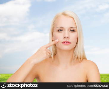 health and beauty concept - face of beautiful young woman pointing at her cheek