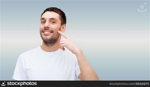 health and beauty concept - smiling young handsome man pointing to cheek