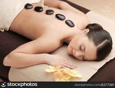 health and beauty, resort and relaxation concept - asian woman in spa salon getting massage with hot stones