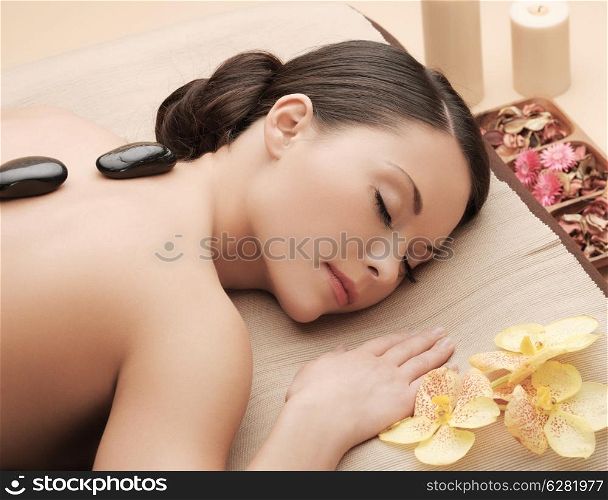 health and beauty, resort and relaxation concept - asian woman in spa salon getting massage with hot stones