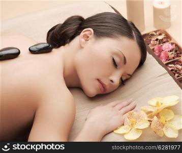 health and beauty, resort and relaxation concept - asian woman in spa salon getting massage with hot stones