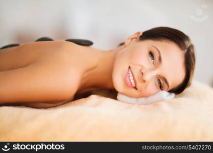 health and beauty, resort and relaxation concept - beautiful woman in spa salon with hot stones