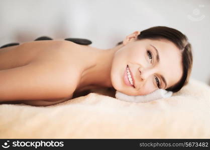 health and beauty, resort and relaxation concept - beautiful woman in spa salon with hot stones