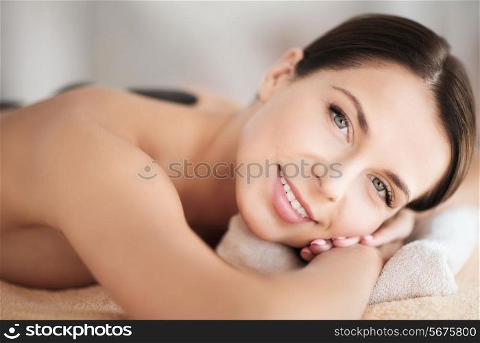 health and beauty, resort and relaxation concept - beautiful woman in spa salon with hot stones