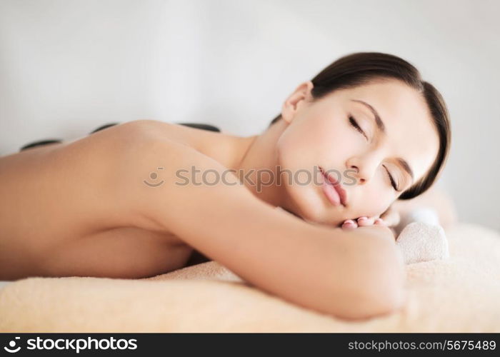 health and beauty, resort and relaxation concept - beautiful woman with closed eyes in spa salon with hot stones