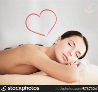 health and beauty, resort and relaxation concept - beautiful woman with closed eyes in spa salon with hot stones