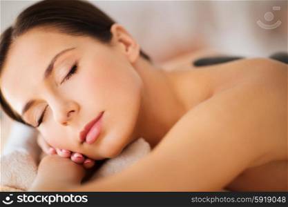 health and beauty, resort and relaxation concept - beautiful woman with closed eyes in spa salon with hot stones
