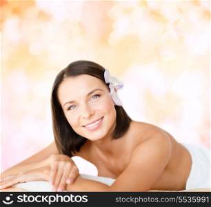 health and beauty, resort and relaxation concept - beautiful woman with flower in her hair in spa salon lying on the massage desk