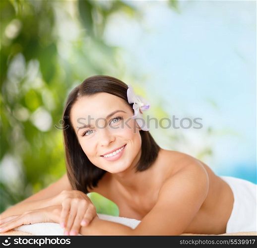health and beauty, resort and relaxation concept - beautiful woman with flower in her hair in spa salon lying on the massage desk