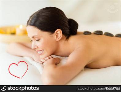health and beauty, resort and relaxation concept - smiling woman in spa salon with hot stones