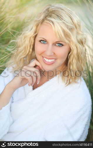 Health and beauty spa concept shot of a beautiful blond haired young woman sitting amongst tall grass and wearing a white towelling bath robe