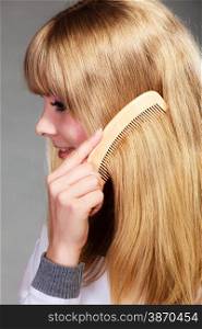 Health beauty and haircare concept - Closeup young blonde woman refreshing her hairstyle she combing her long hair with wooden comb, closeup
