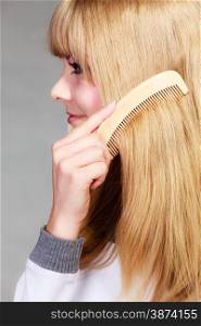 Health beauty and haircare concept - Closeup young blonde woman refreshing her hairstyle she combing her long hair with wooden comb, closeup
