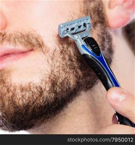 Health beauty and skin care concept. Closeup of male face. Young man guy styling beard holding disposable blue razor blade.