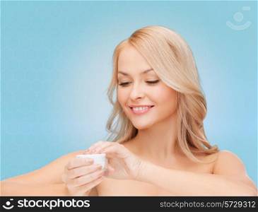 health, beauty and spa concept - smiling young woman opening cream over blue background