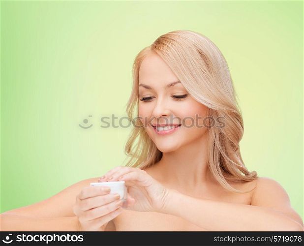 health, beauty and spa concept - smiling young woman opening cream over green background