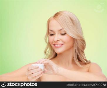 health, beauty and spa concept - smiling young woman opening cream over green background