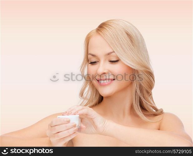 health, beauty and spa concept - smiling young woman opening cream over pink background